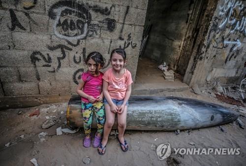 이스라엘군이 쏜 불발탄 위에 앉은 가자지구의 팔레스타인 자매. [사진=EPA/연합뉴스]